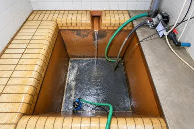 A tiled water tank being refilled by hose after cleaning, with a submersible pump at the bottom.