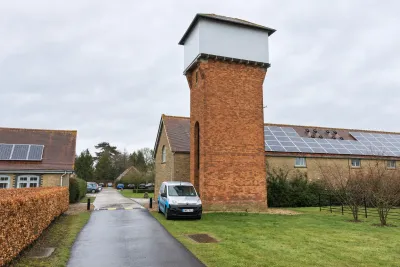 A red brick water tower beside a barn with solar panels, with an Invicta van on the drive.