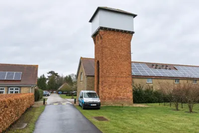 A red brick water tower beside a barn with solar panels, with an Invicta van on the drive.
