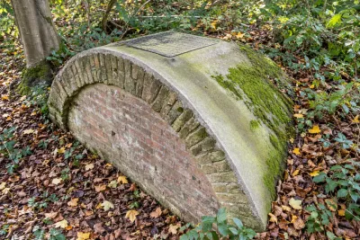 An old brick-domed water tank with a mossy cover, set in woodland under autumn leaves.