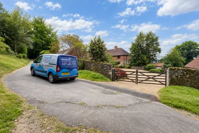 An Invicta van parked on a lane beside a five-bar gate, with a house behind trees.