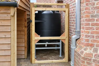 A black storage tank in a timber-framed enclosure against a brick wall.
