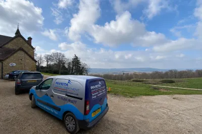 An Invicta van on the gravel drive of a stone country house, with a view across the Weald behind.