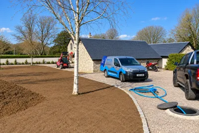 A newly built stone house with an Invicta van on the drive and fresh groundworks, blue pipe coiled on the gravel.