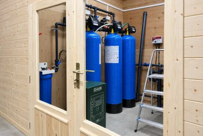 Seen through a timber doorway, a plant room with blue pressure vessels, a booster pump set and a step ladder.