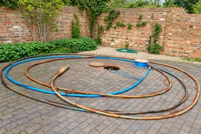 A walled courtyard with the borehole chamber open and the rising main coiled out across the block paving.