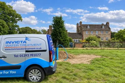 An Invicta van on the lawn of a stone manor house, with drilling spoil and a borehole hose behind it.