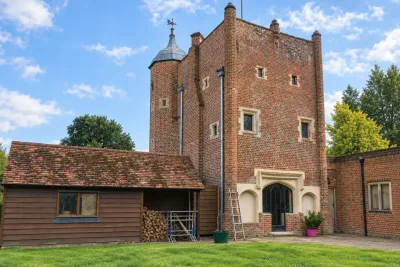 A Tudor brick tower with a lawn and a timber outbuilding beside it.