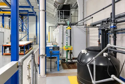 An industrial plant floor with black tanks, a blue steel mezzanine and overhead pipework.