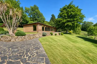 A timber garden pavilion across a lawn, with a terrace and mature trees.