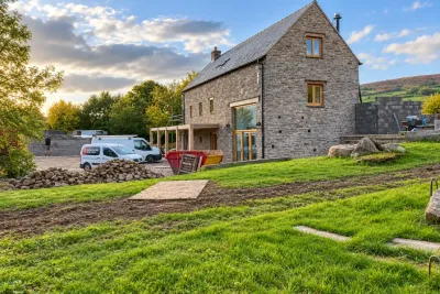 A stone house being renovated, with a van and skip on the drive and hills behind.